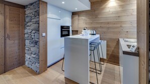 Une cuisine moderne avec des poutres en bois, un mur d’accent en pierre et un four encastré.