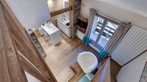 Une cuisine moderne dotée d’un îlot central, d’un coin repas avec une table et des chaises blanches, d’un mur d’accent en pierre et d’une vue sur l’extérieur grâce à une porte vitrée.