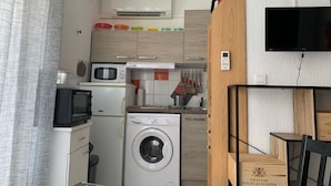Een compacte keuken met een wasmachine, magnetron en een kleine koelkast.