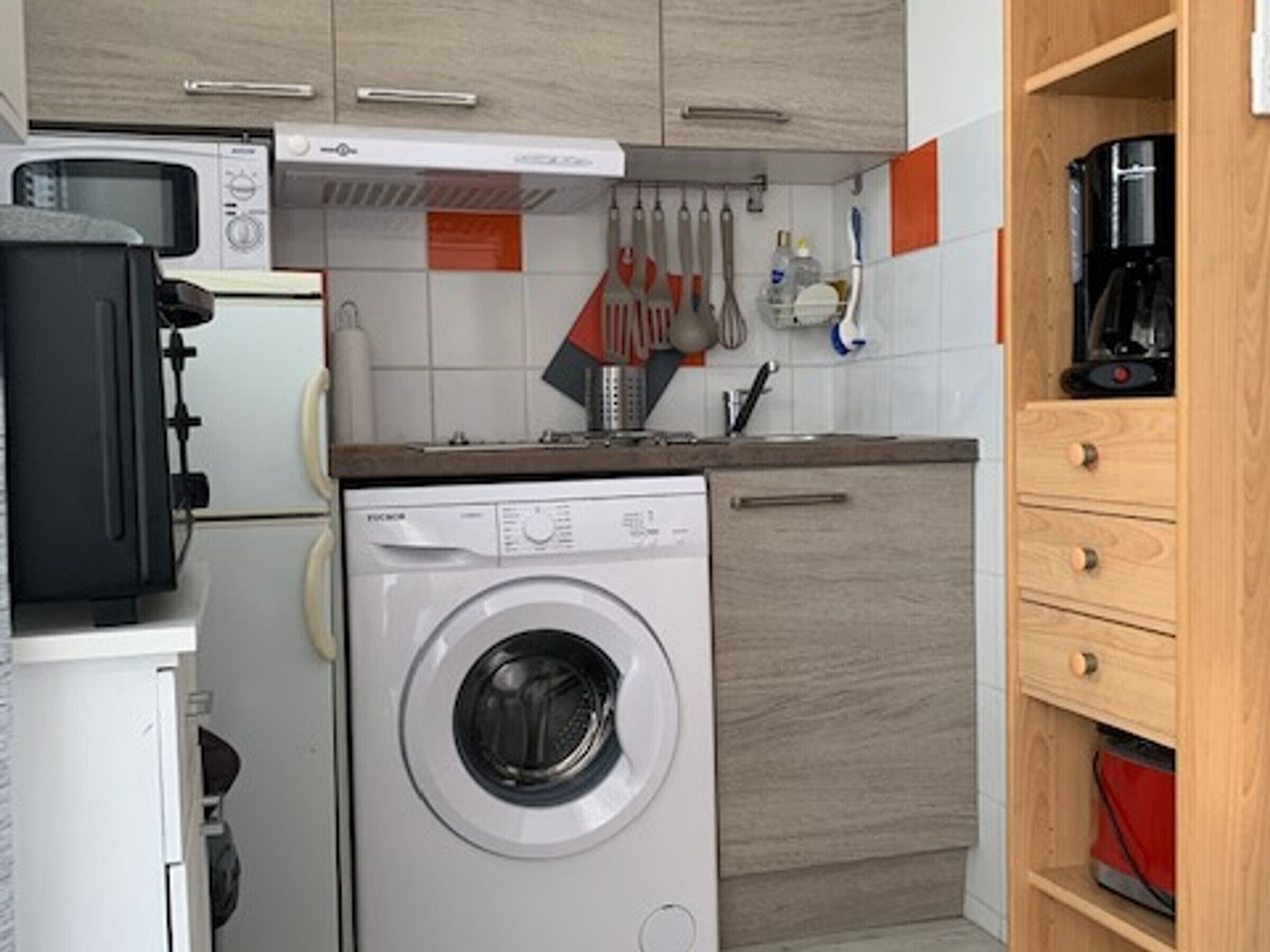 A compact kitchen with a washing machine, microwave, and coffee maker.
