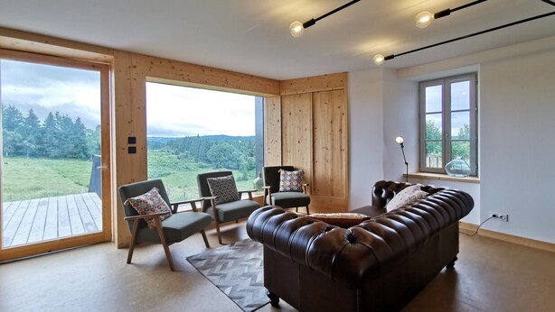 A spacious room with a large window offering a view of a forested area. There is a leather sofa, two armchairs, and a wooden floor. - Nature Retreat: Cozy Cottage with Panoramic Views, Perfect for Family & Friends Near Lyon & Clermont-Ferrand (Saint-Victor-sur-Arlanc)
