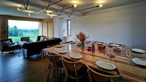 A dining area with a wooden table set for four, surrounded by chairs, and a sofa in the background. - Nature Retreat: Cozy Cottage with Panoramic Views, Perfect for Family & Friends Near Lyon & Clermont-Ferrand (Saint-Victor-sur-Arlanc)