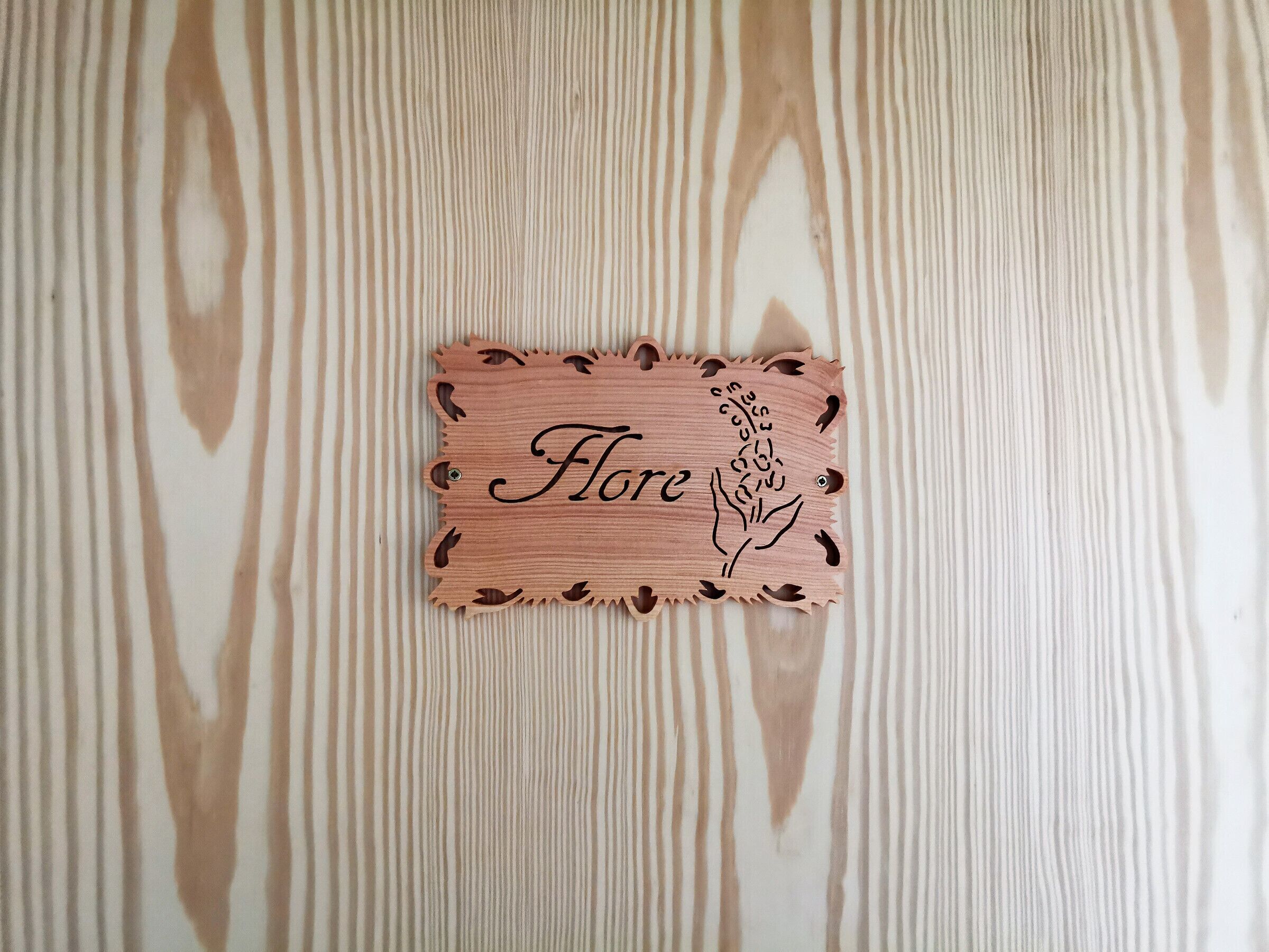 Una placa de madera con la palabra 'Flore' y un diseño floral sobre un fondo a rayas.