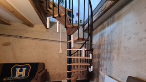 Une pièce avec un sol à carreaux noirs et blancs, un escalier en bois avec des rampes noires, un canapé orné du logo d’une équipe sportive et un mur uni avec une prise de courant.