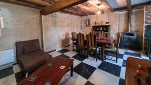 Une pièce chaleureuse avec un sol à carreaux, des poutres apparentes, une table à manger avec des chaises, un canapé et un téléviseur.