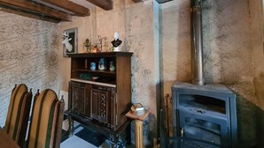 Une pièce rustique avec des poutres apparentes, un poêle d’époque et un buffet en bois agrémenté d’objets décoratifs.