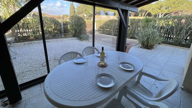 A patio with a round table and chairs, a bottle of wine, and a glass. - Spacious Home with Pool, Tennis, and Garden - Sleeps 10 (Vendres)