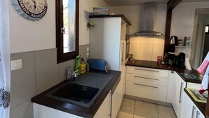 A compact kitchen with a sink, countertop, and basic appliances. A decorative clock is mounted on the wall, and a window provides natural light. - Spacious Home with Pool, Tennis, and Garden - Sleeps 10 (Vendres)