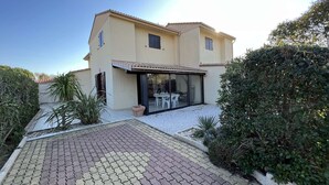 A two-story house with a patio area, a covered outdoor seating space, and a gravel driveway. - Spacious Home with Pool, Tennis, and Garden - Sleeps 10 (Vendres)