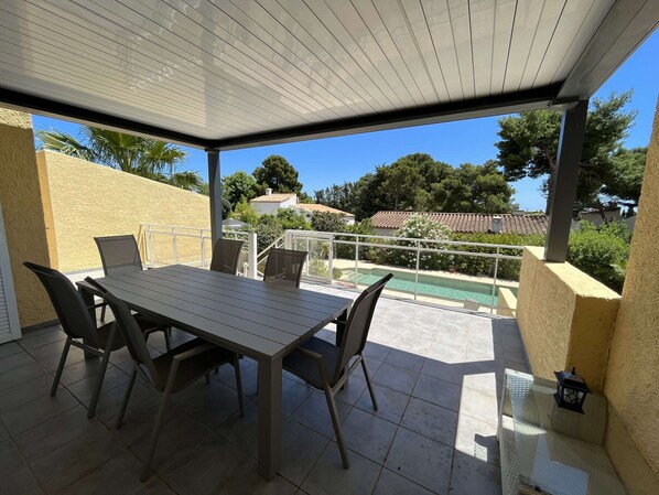 An outdoor patio with a table and chairs, a pool, and a view of the surrounding area.