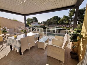 An outdoor patio area with wicker furniture, a glass table, and potted plants.