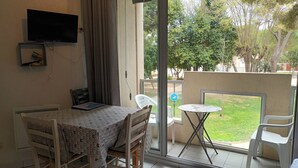 Une pièce comprenant une table à manger, des chaises, une petite table ronde et un téléviseur fixé au mur.