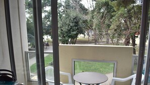 Un balcon avec une table et deux chaises, donnant sur un espace vert arboré où est garé un scooter.