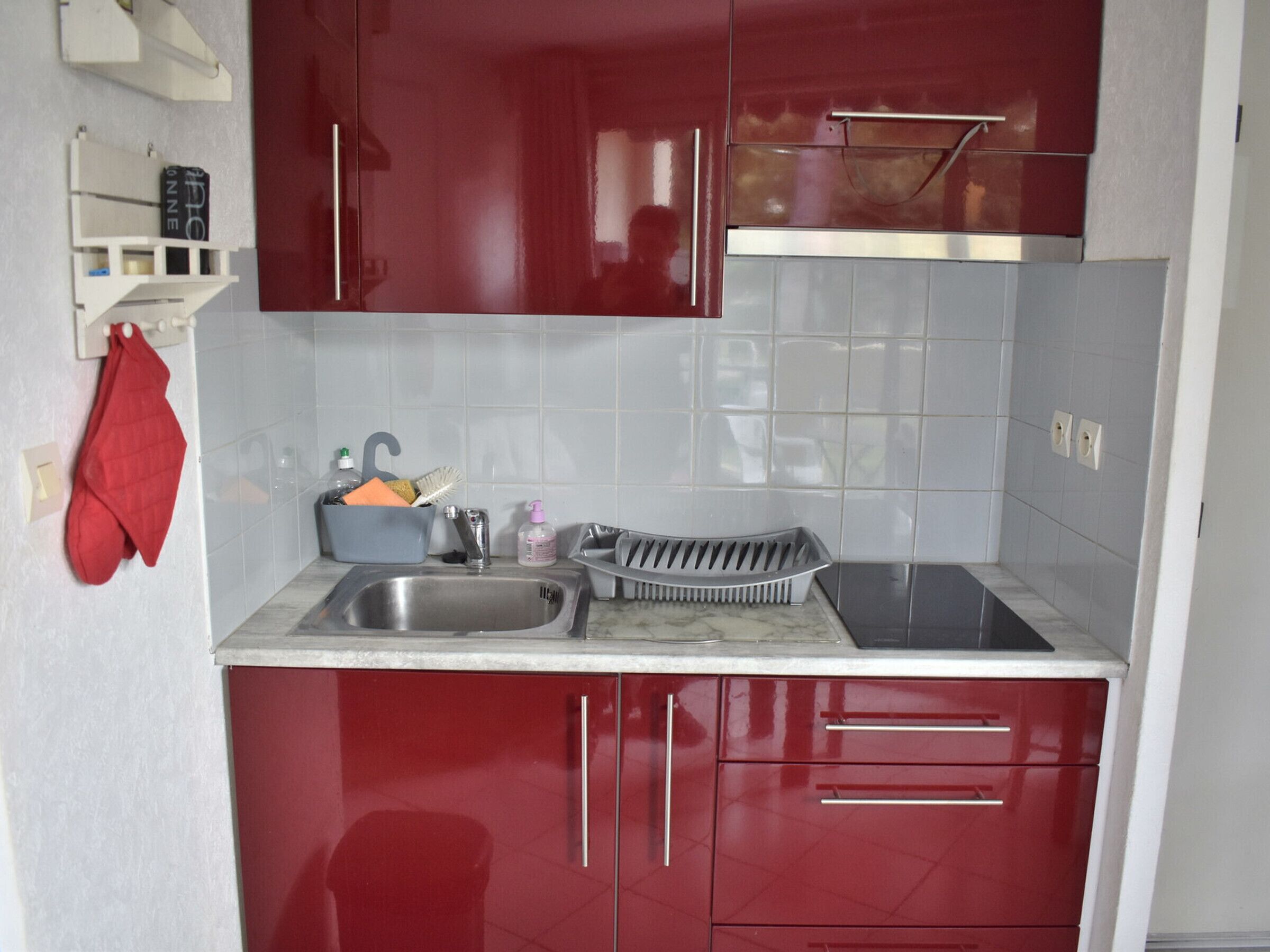 Une cuisine compacte avec des meubles rouges, un évier en acier inoxydable et un four encastré.
