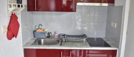 Une cuisine compacte avec des meubles rouges, un évier en acier inoxydable et un four encastré.