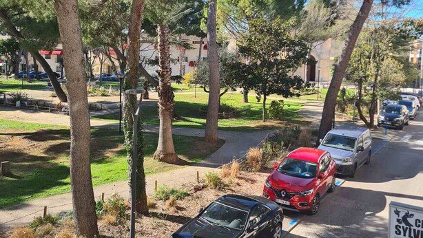 Un espace de stationnement avec des voitures, des arbres et un beffroi en arrière-plan.