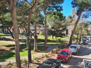 Un espace de stationnement avec des voitures, des arbres et un beffroi en arrière-plan.