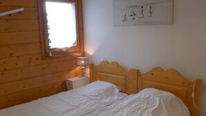 Een kamer met houten lambrisering, een bed, een nachtkastje, een lamp en een raam.