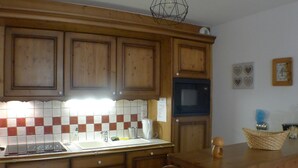 Een keuken met houten kastjes, een betegelde achterwand, een magnetron en een spoelbak.