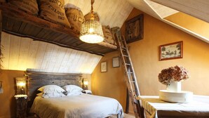 Ein gemütliches Schlafzimmer mit Holzbalkendecke, einem Bett mit weißer Bettwäsche, einem Holzstuhl und einem Tisch mit Blumen in einer Vase.