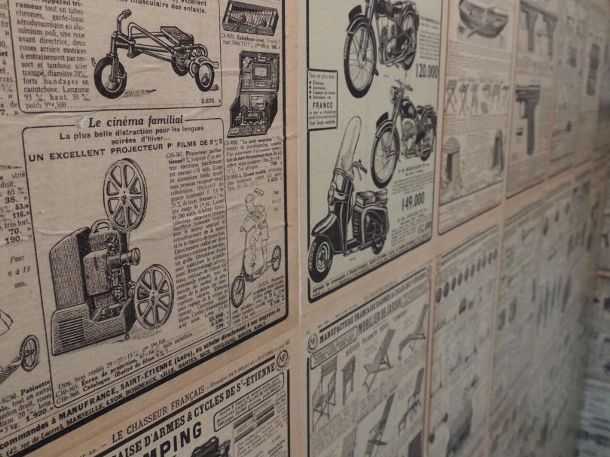 A wall of vintage advertisements featuring various products like bicycles, motorcycles, and a cinema projector.