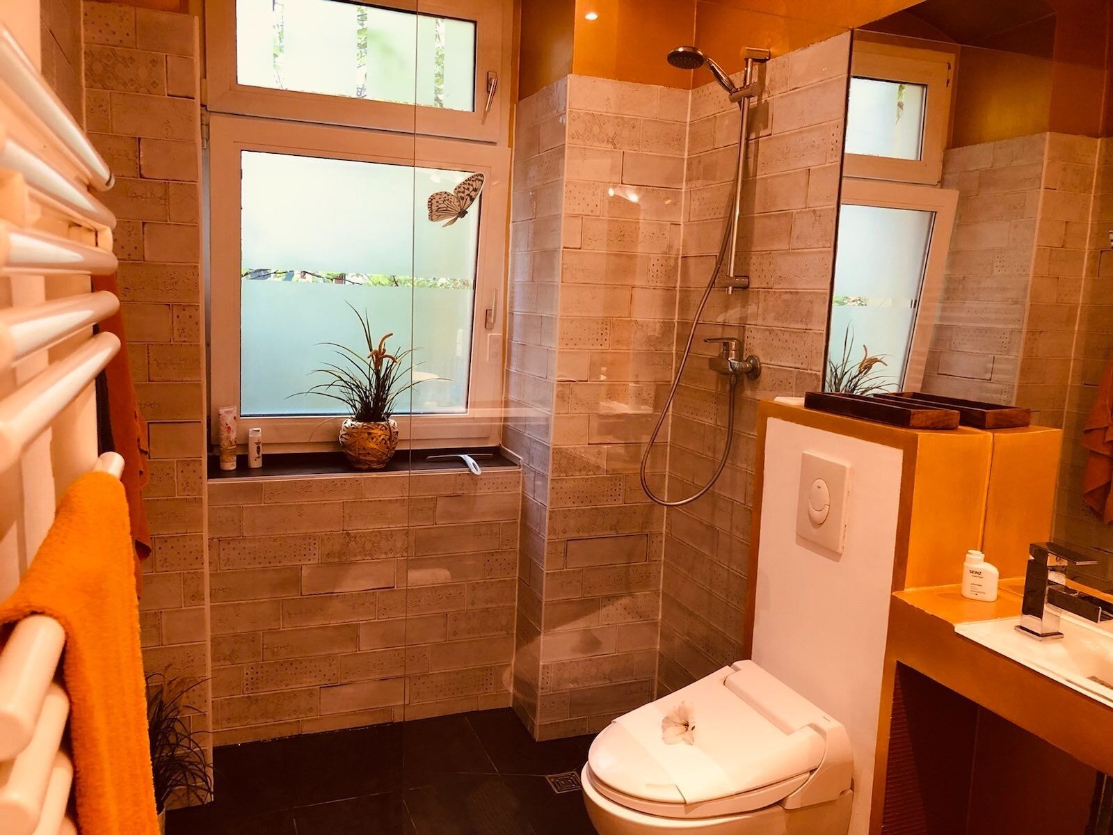 Un baño con inodoro, ducha y ventana decorada con una mariposa.