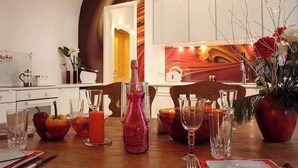 Une cuisine moderne avec des meubles blancs, une table à manger dressée avec de la verrerie et un centre de table, ainsi qu’une œuvre d’art murale abstraite et colorée.
