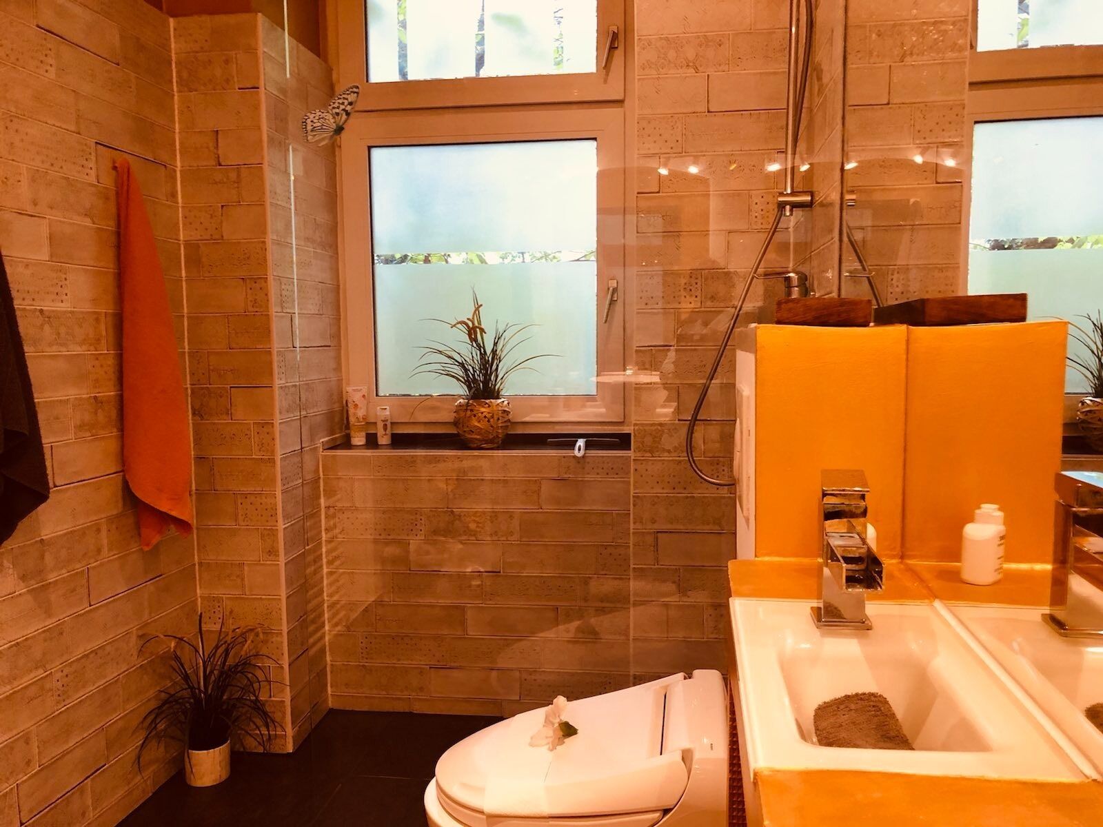 Ein modernes Badezimmer mit Dusche, Toilette und Waschbecken. Zwei Blumentöpfe und ein Handtuchhalter sind vorhanden.