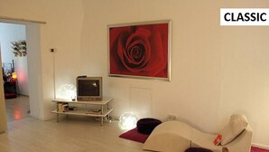Un salon avec une télévision, un tableau représentant une rose rouge et un canapé avec une étiquette.