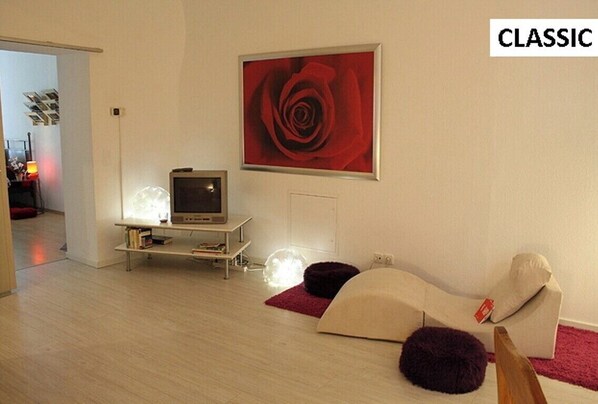 Een woonkamer met een televisie, een schilderij van een rode roos en een bank met een prijskaartje.