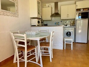 Une cuisine compacte avec des meubles blancs, un lave-linge encastré, un four à micro-ondes et un coin repas comprenant une table et des chaises.