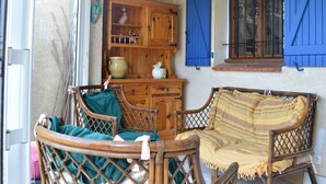 A cozy room with wicker furniture, a wooden cabinet, and blue shutters. - 4 Bedroom Villa, Sleeps 6, 800m from Beach, Parking, Verandas, Pets Allowed (Fleury-Saint-Pierre-la-Mer)