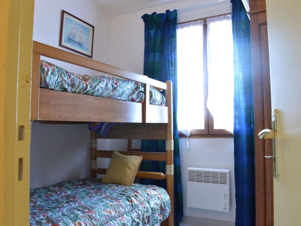 Une chambre avec un lit superposé, une fenêtre, des rideaux et un radiateur.