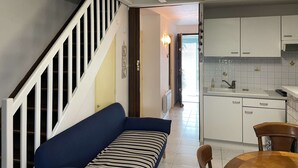 A compact living space with a staircase, a sofa, a dining table, and a kitchen area. - 4 Bedroom Villa, Sleeps 6, 800m from Beach, Parking, Verandas, Pets Allowed (Fleury-Saint-Pierre-la-Mer)