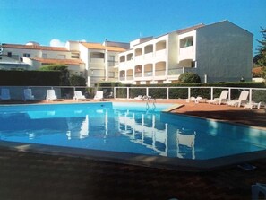 Une piscine avec des chaises longues, un ciel bleu dégagé et un bâtiment doté de balcons en arrière-plan.