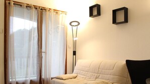 A room with a beige sofa, a floor lamp, and a window with sheer curtains.