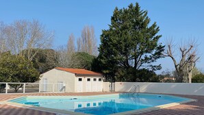 A rectangular swimming pool with a tiled deck, a metal ladder, and a building with a red roof in the background.