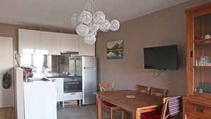 A compact kitchen with modern appliances, a dining area with wooden furniture, and a mounted TV.
