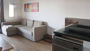 A modern living room with a beige sofa, a dining table, and a kitchen area with a stove.