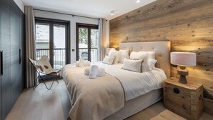 Une chambre à coucher moderne avec un grand lit, une chaise, une tête de lit en bois et une table de chevet avec une lampe.