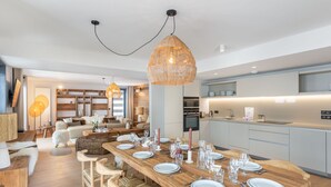 Une cuisine moderne avec une table à manger en bois pouvant accueillir six personnes, un grand îlot central et des appareils électroménagers intégrés.