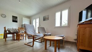 A spacious living area with a wooden floor, a dining table with chairs, a television, and a wooden cabinet. - Quiet house, 3 rooms, garden, WiFi - La Brée-les-Bains (La Brée-les-Bains)