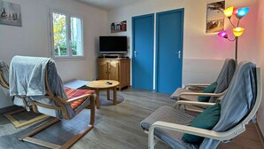 A room with two reclining chairs, a small table, a television on a cabinet, and a pair of blue doors. - Quiet house, 3 rooms, garden, WiFi - La Brée-les-Bains (La Brée-les-Bains)