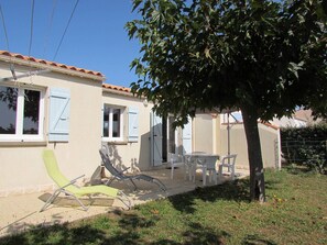 A house with a tiled roof, a patio with chairs, and a tree providing shade. - Quiet house, 3 rooms, garden, WiFi - La Brée-les-Bains (La Brée-les-Bains)