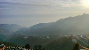 A panoramic view of a mountainous landscape with scattered buildings. - 360 Degree View Homestay (Dehradun)