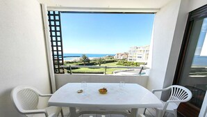 Ein Balkon mit weißem Tisch und Stühlen, Blick auf das Meer und Gebäude im Hintergrund.