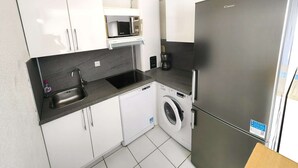 Eine kleine Küche mit weißen Schränken, einem Edelstahl-Kühlschrank, einer Waschmaschine und einer Mikrowelle.