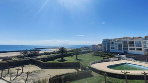 Ein sonniger Tag an einem Küstenort mit Pool, Strand und modernen Gebäuden.