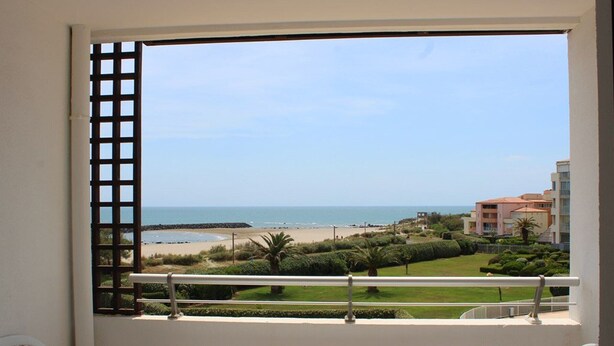 Ein Balkon mit Tisch und Stühlen, mit Blick auf einen Strand und einen gepflegten Garten, der einen klaren Meerblick bietet.