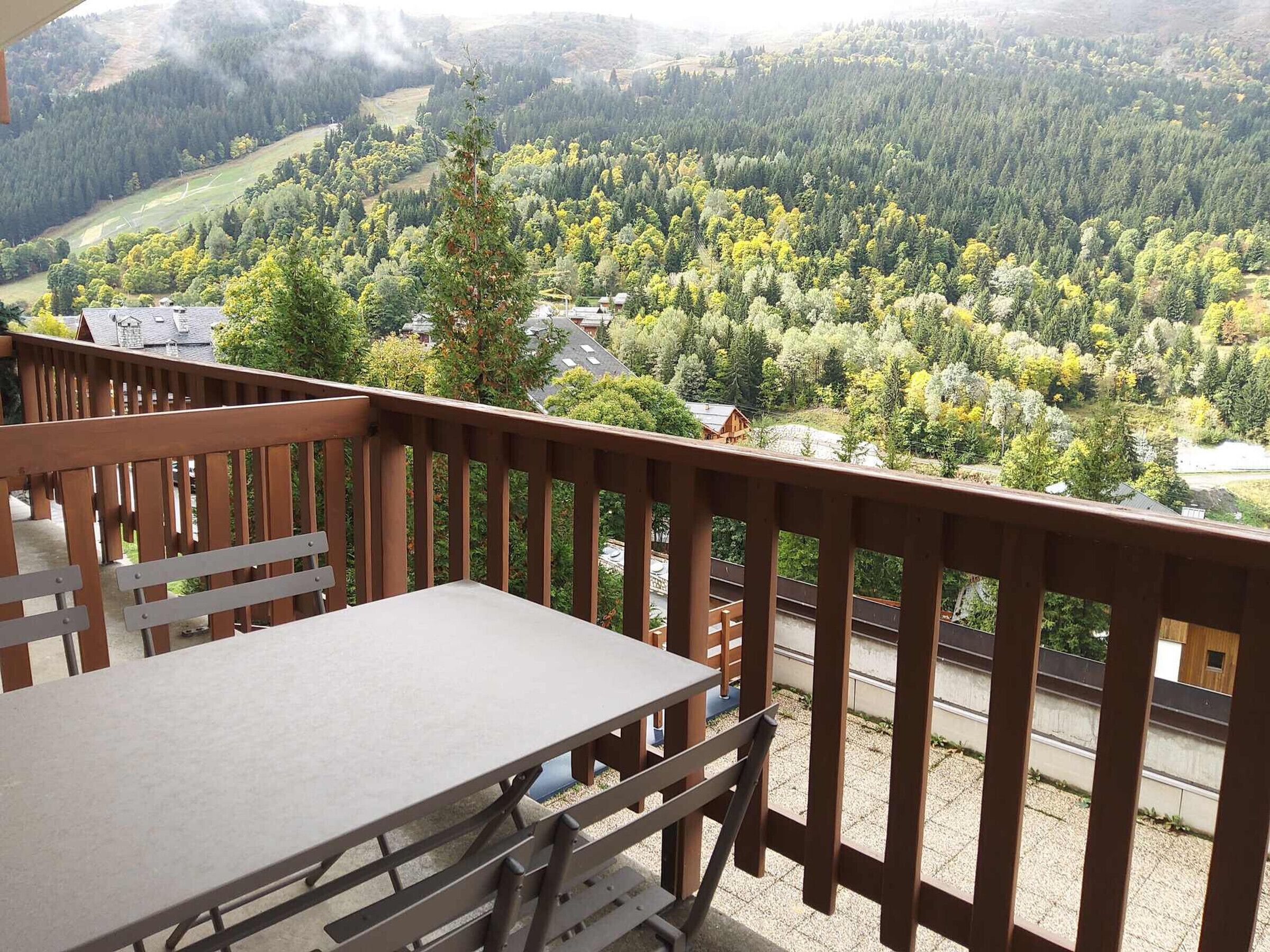 A balcony with a table and chairs overlooking a forested valley.